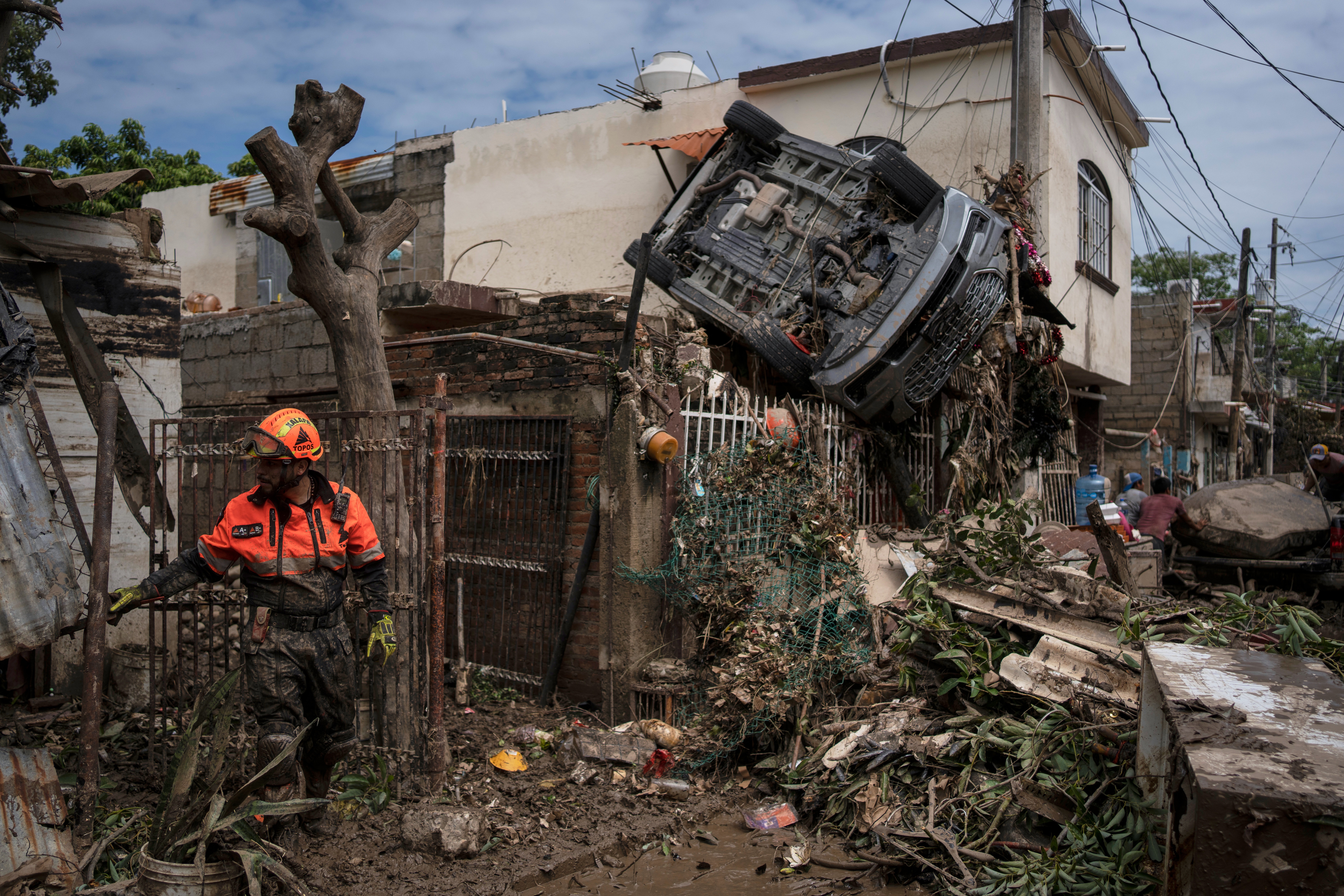 A rescue worker, part of the volunteer brigade known as the Topos, works near a car hanging over a fence by a damaged house in Poza Rica, Mexico, Monday, Oct. 13, 2025, after torrential rains.